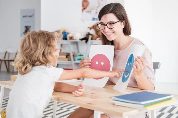 Professional educational counselor helping a young child identify emotions using visual learning cards during an educational counseling session in Lahore to support emotional, social, and academic development.