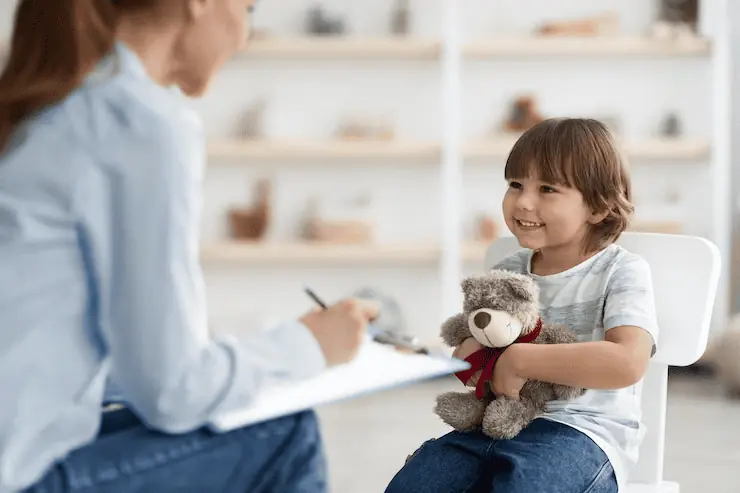 Young child smiling during a child counseling session in Lahore while holding a teddy bear and talking with a child psychologist in a safe, supportive, and child-friendly environment.